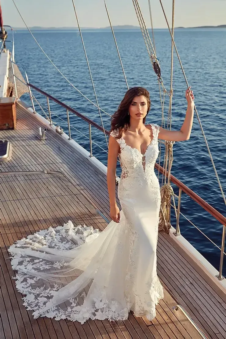 Woman in white wedding dress on a boat, posing with arm raised, with ocean in the background.