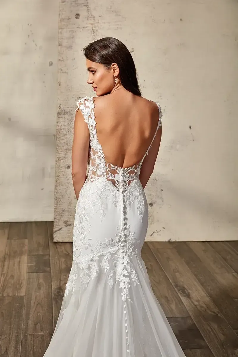 Woman in a white lace wedding dress with a low back, posing indoors.