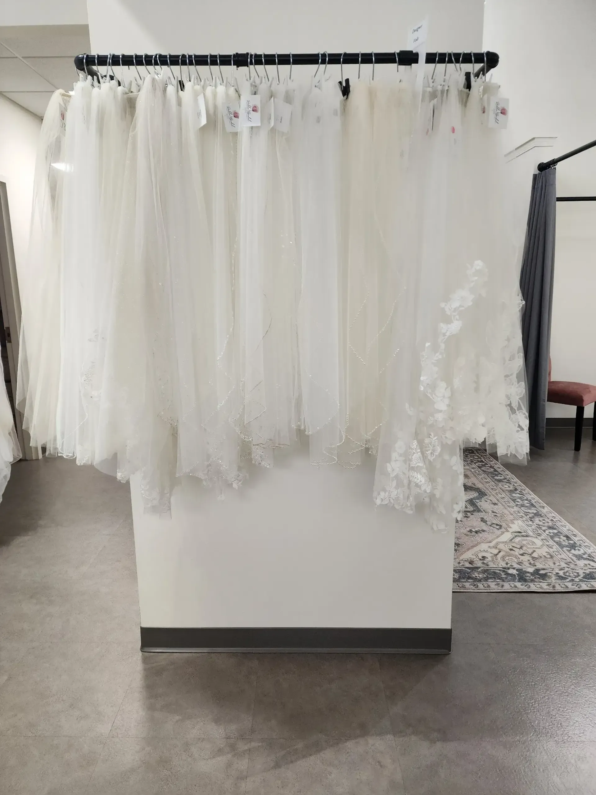 Wedding veils hanging on a rack in a bridal shop, white fabric, neutral setting.