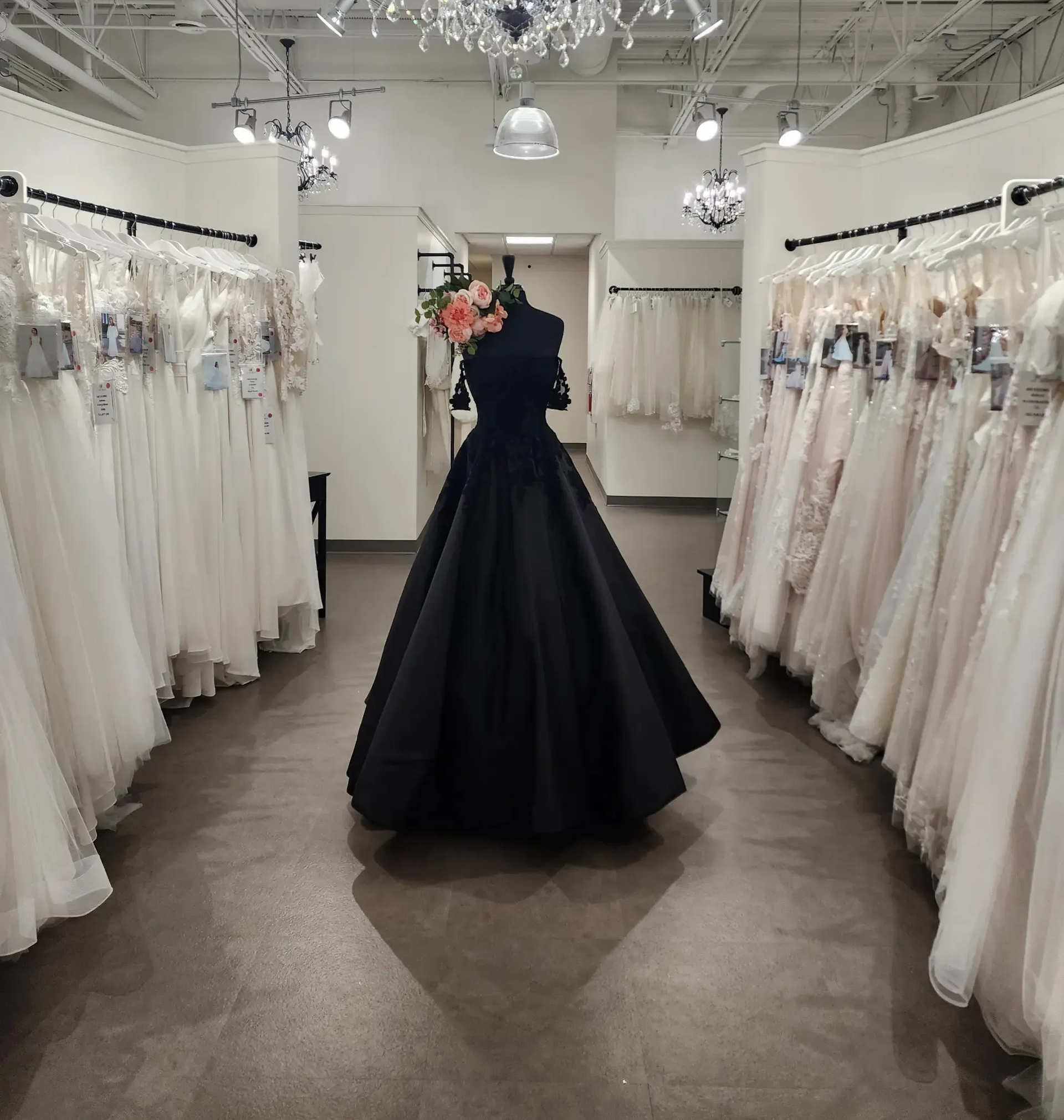 Bridal shop interior: black dress on mannequin, rows of white wedding dresses on racks.