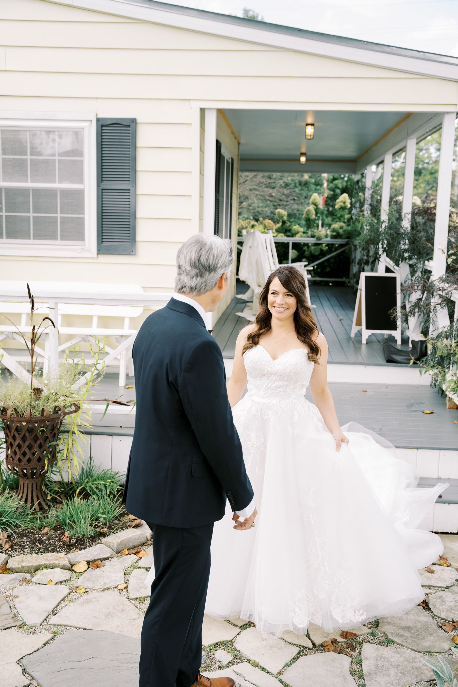 Bride in white dress smiles at man in a dark suit on a porch.