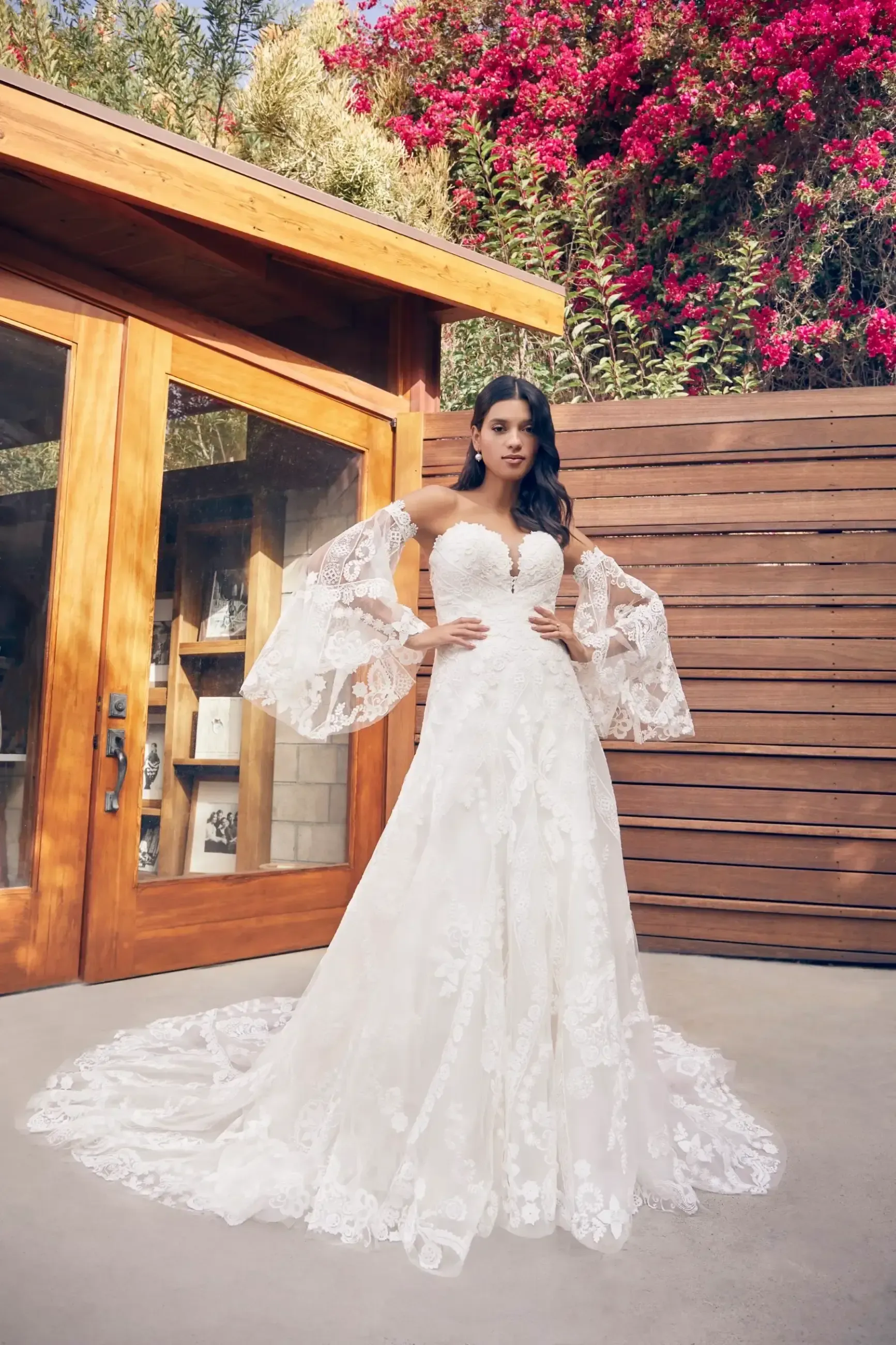 Woman in a white lace wedding dress with bell sleeves, standing outside.