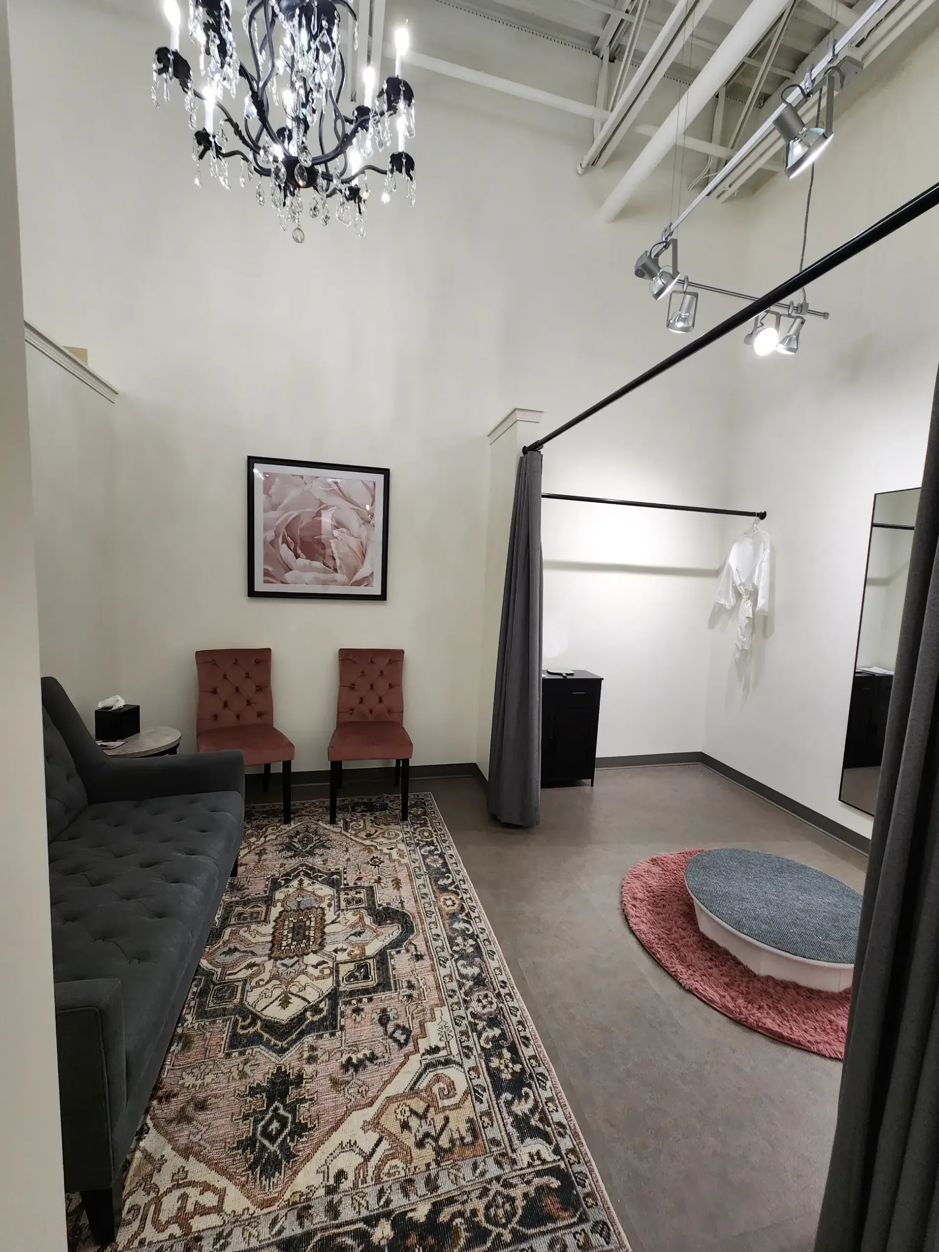 Fitting room interior with sofa, chairs, rug, and chandelier.
