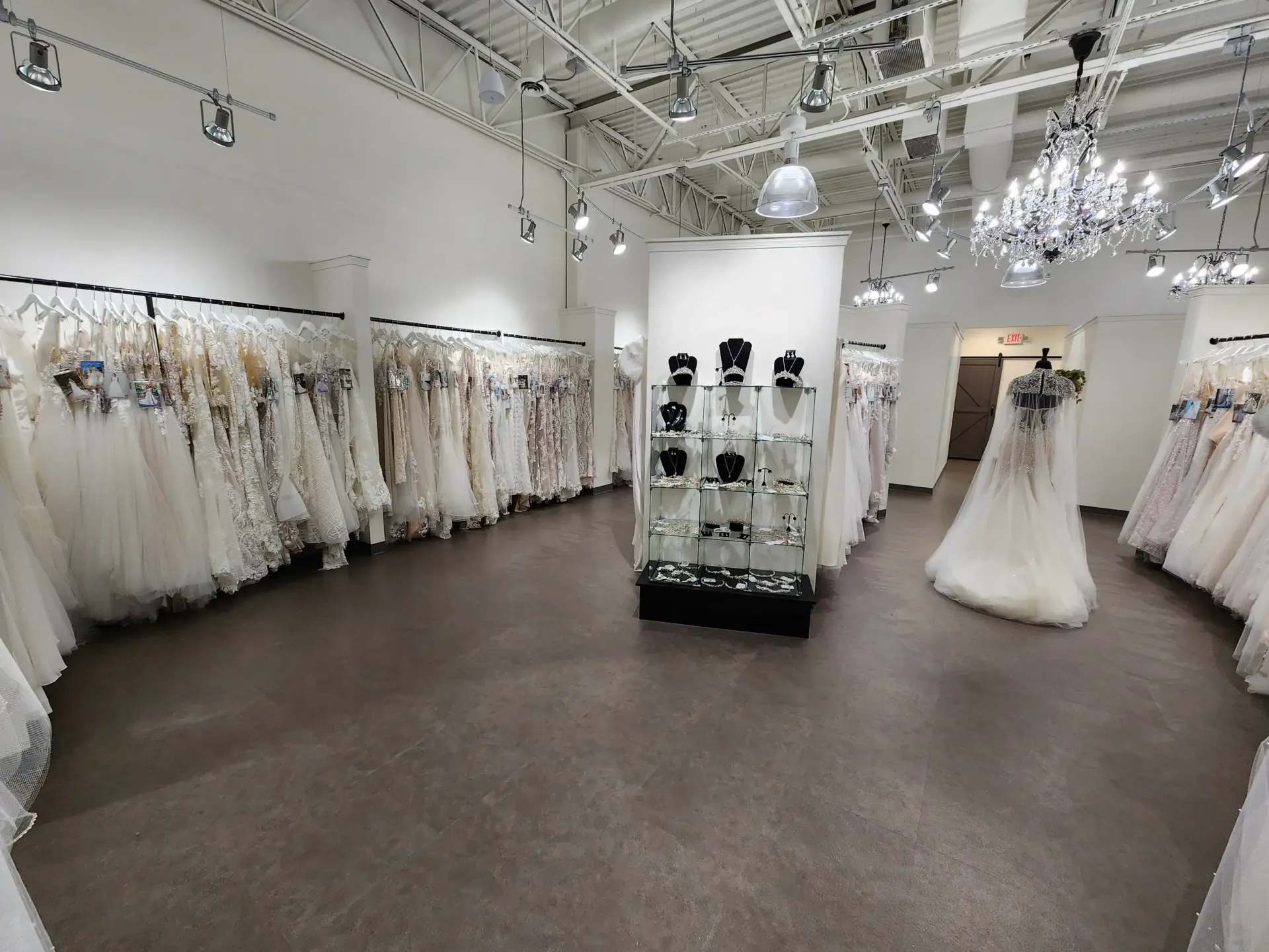 Bridal shop interior with rows of wedding dresses, display case with jewelry, and a mannequin.
