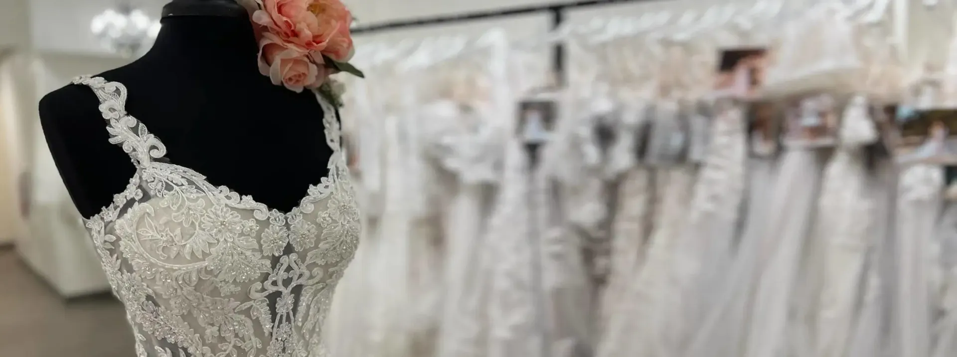 A wedding dress on a black mannequin, with more dresses blurred in the background, in a bridal shop.