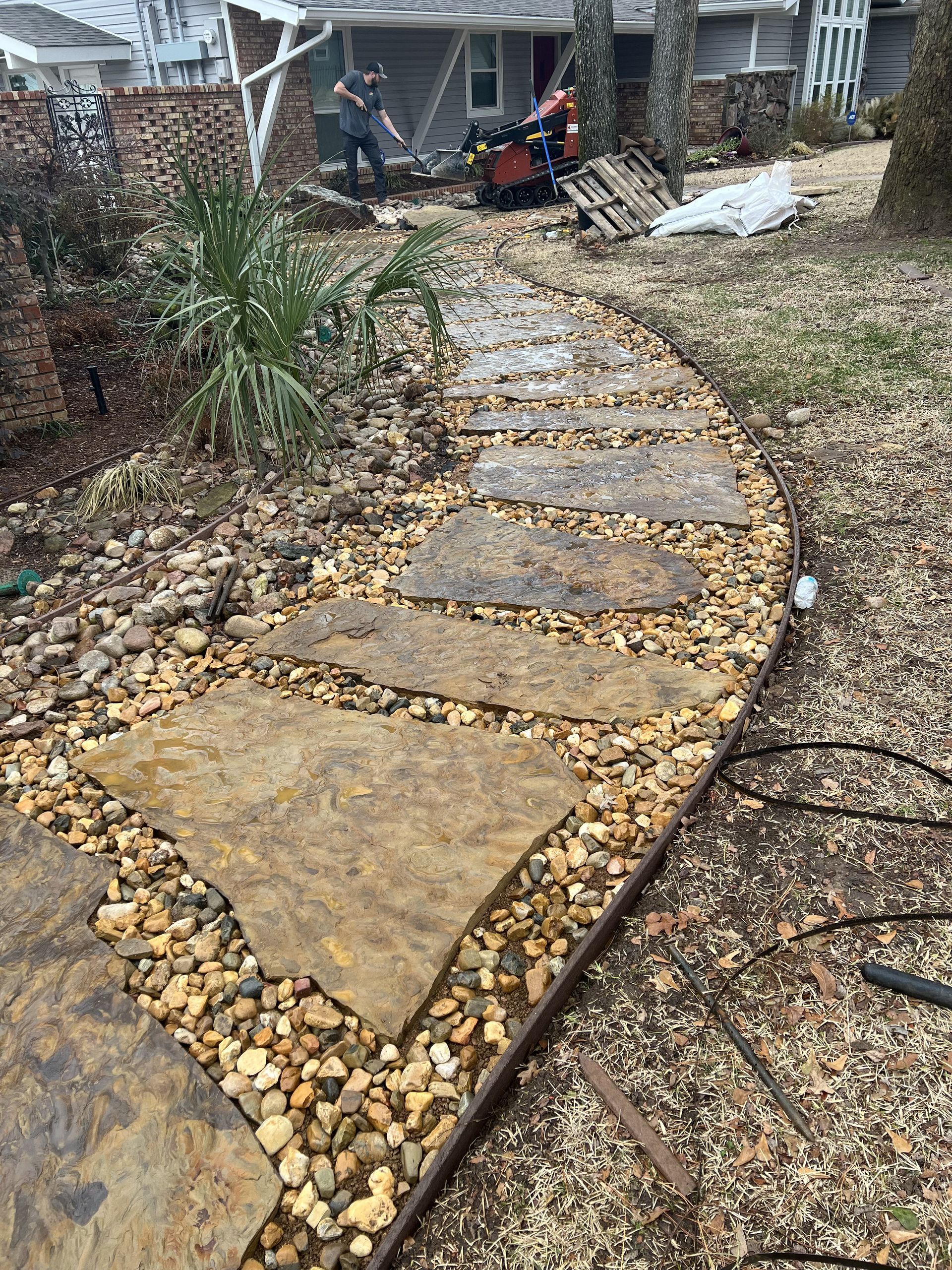 A stone walkway leading to a house with a lawn mower in the background.