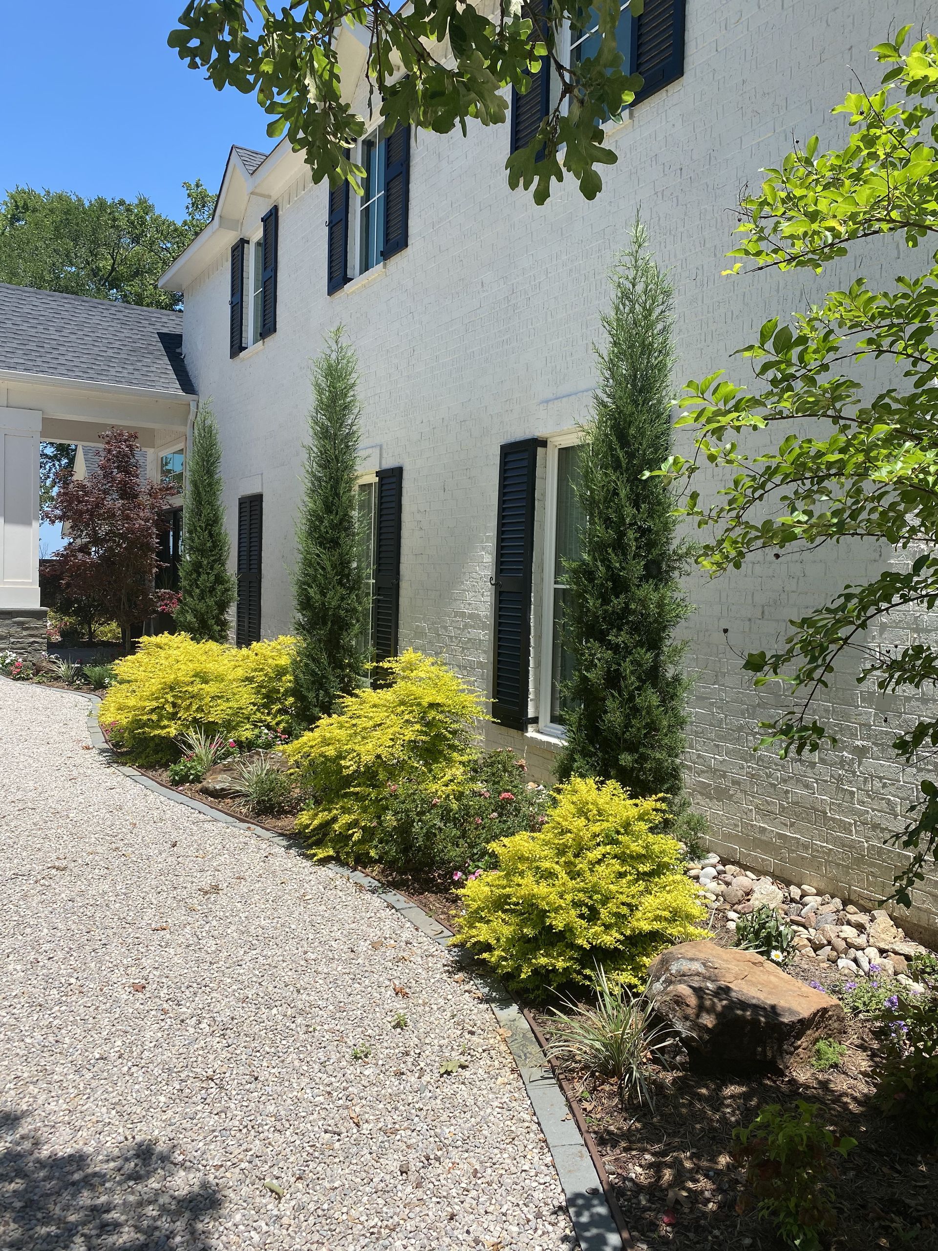 A white house with black shutters and a gravel driveway