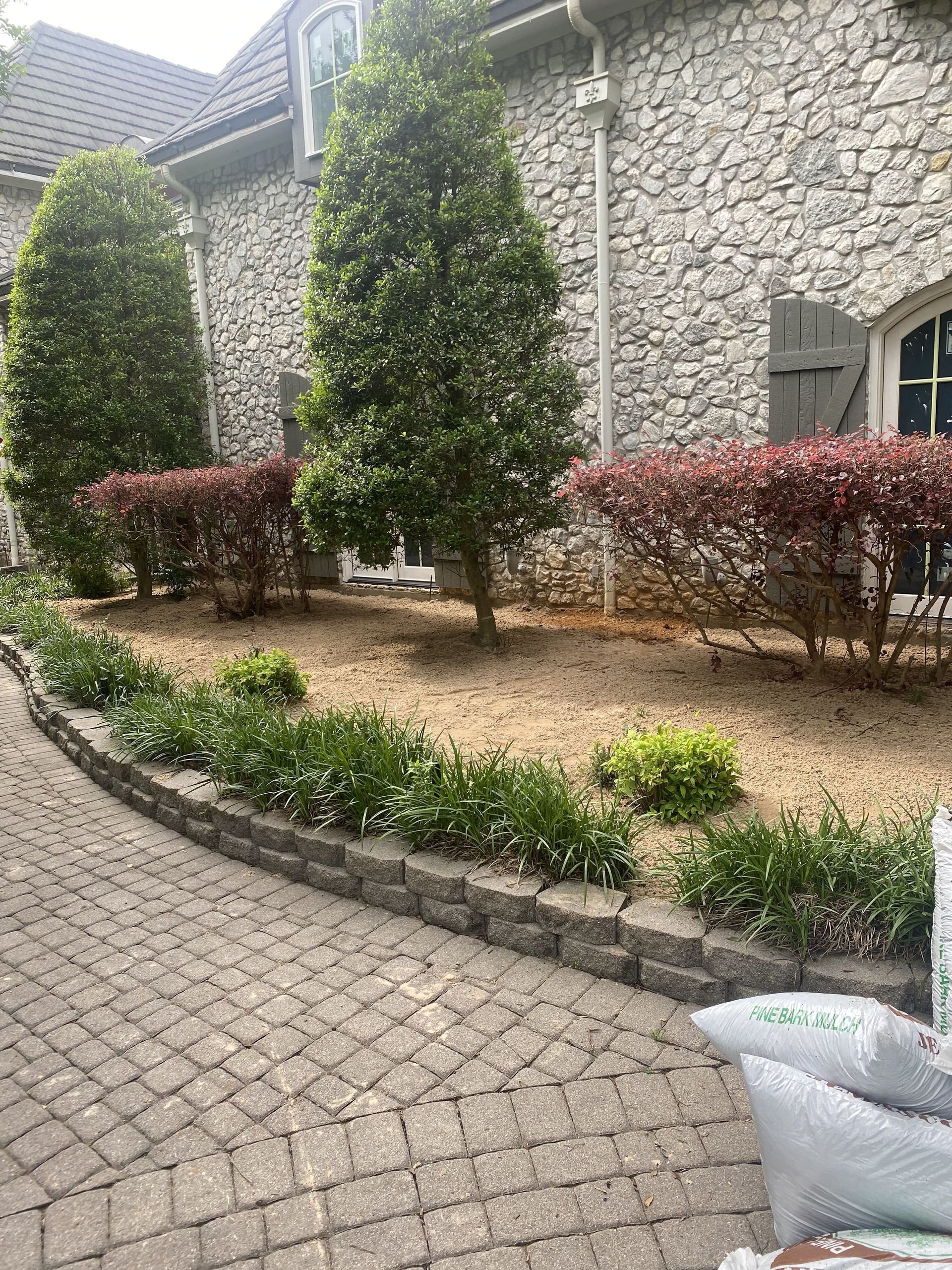 A brick walkway leading to a large stone building with trees and bushes in front of it.