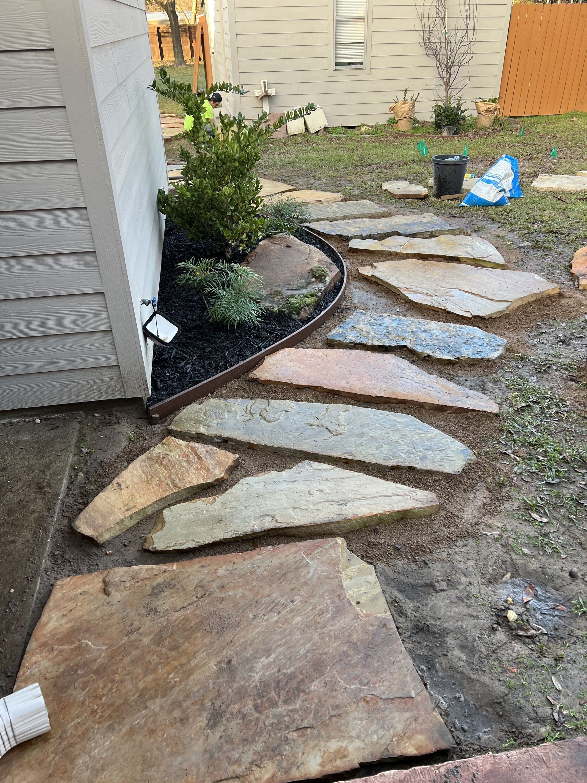 A stone walkway is being built in the backyard of a house.