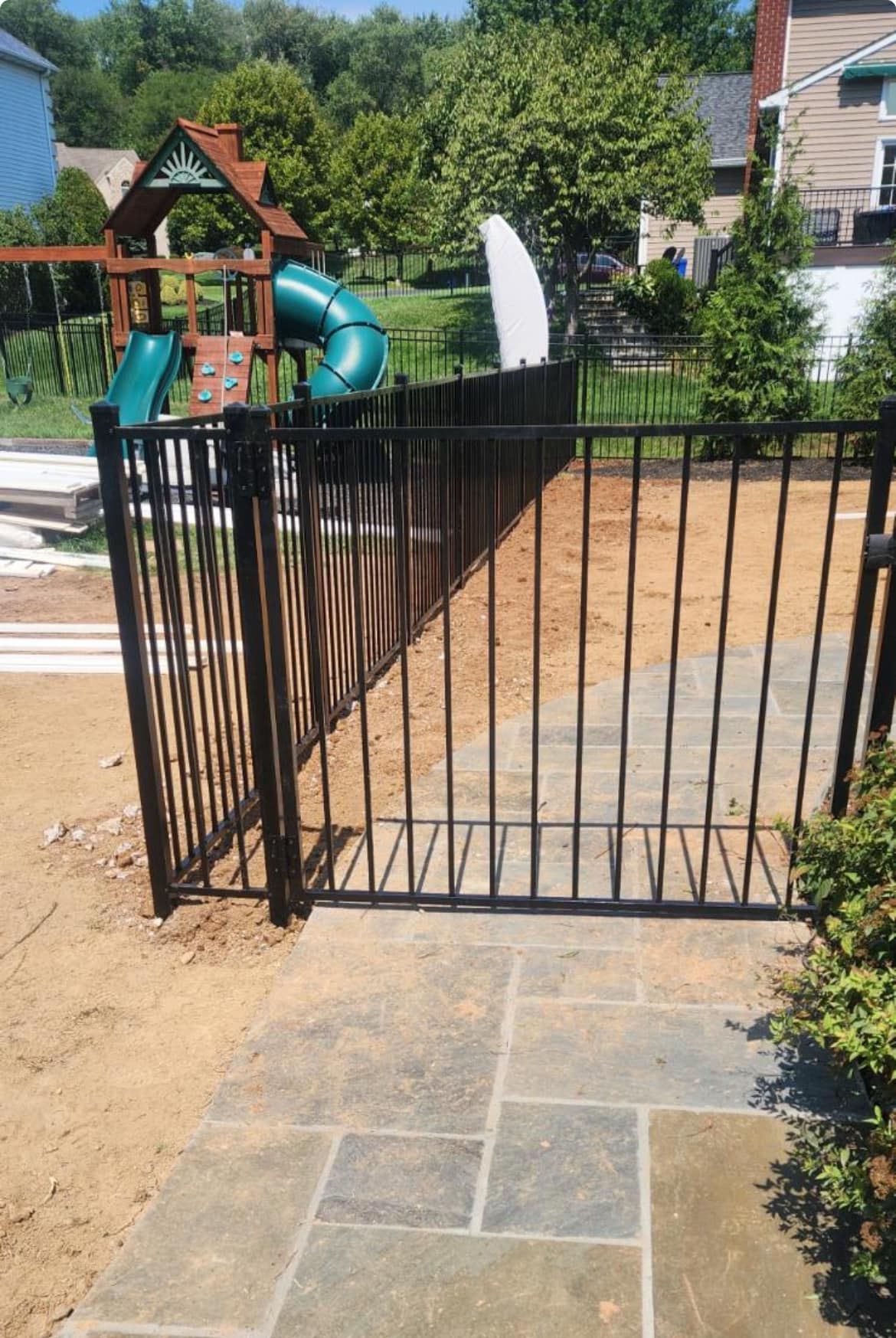 Black metal fence and gate on a stone patio, with a playground visible in the backyard.