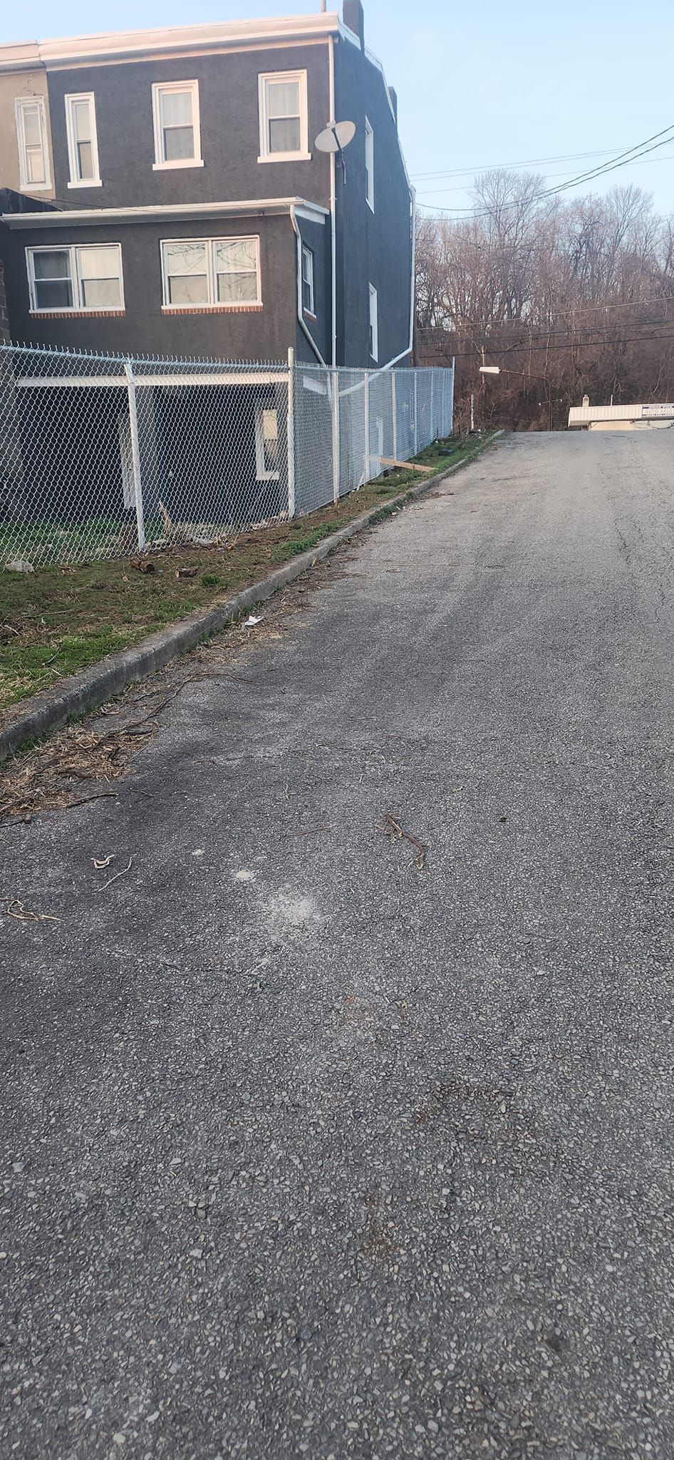 A three-story dark building with a chain-link fence, next to a gravel path.