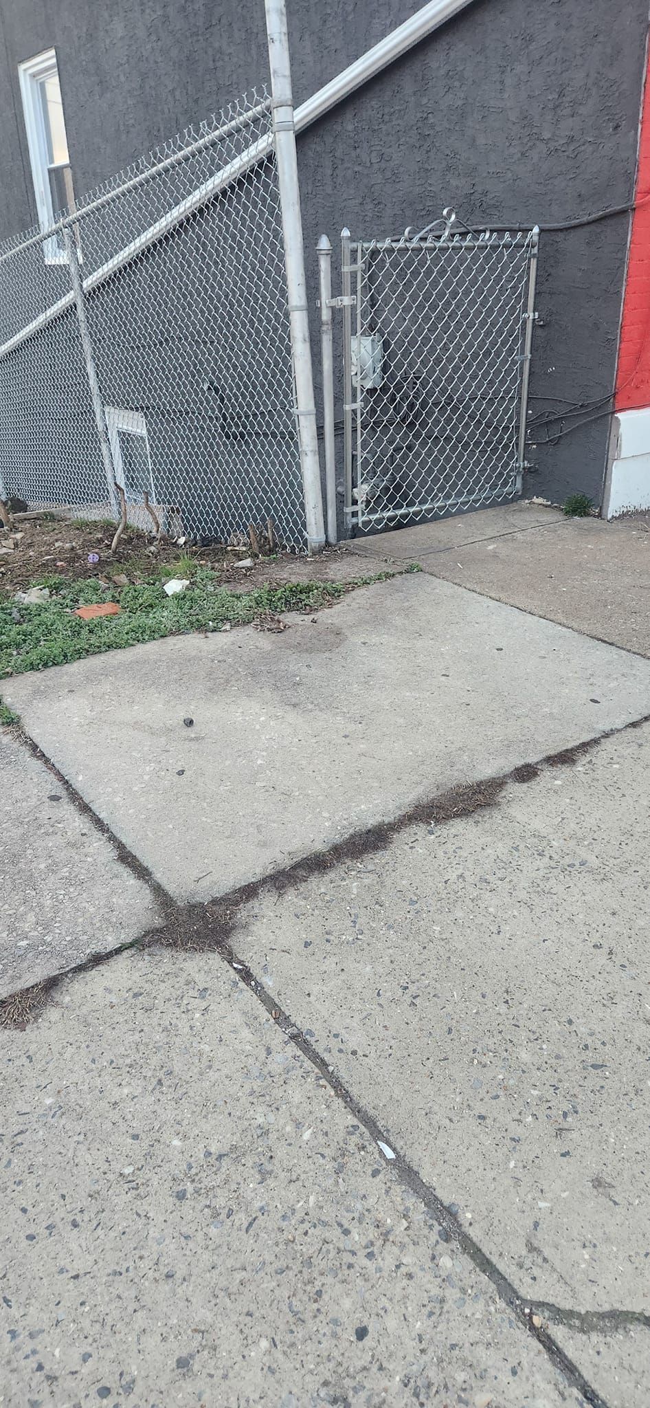 A concrete sidewalk with a rectangular patch of concrete next to a chain-link fence.