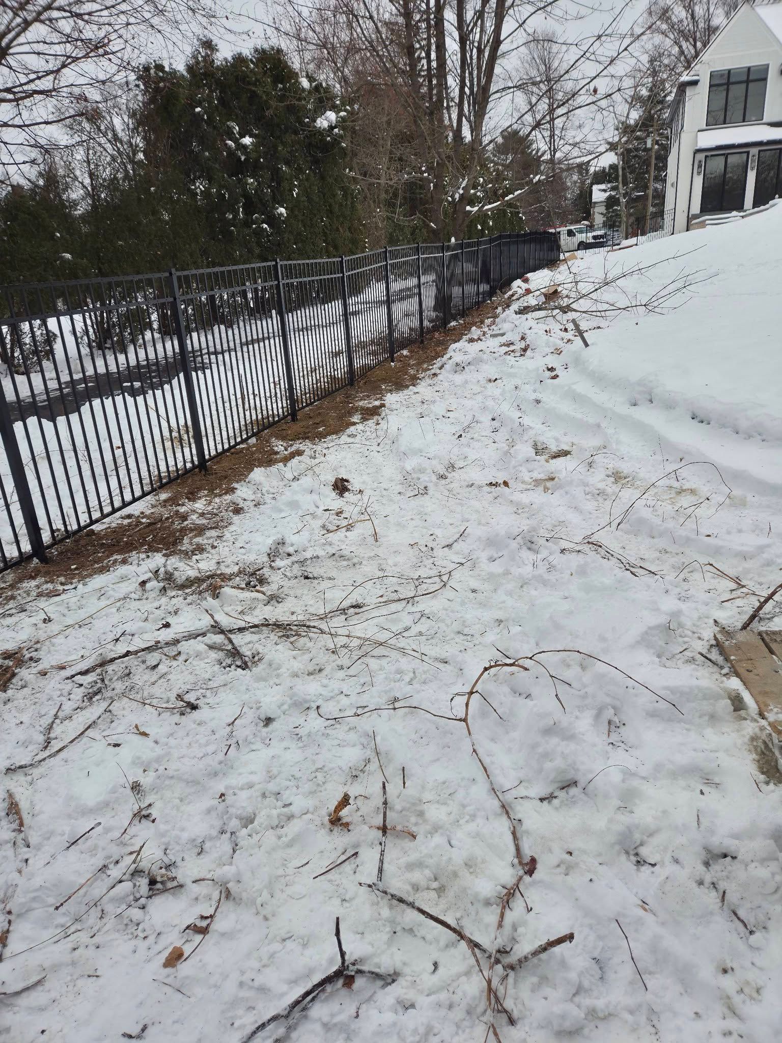 Snowy ground beside a black fence. A house is visible in the background on a slightly sloping hill.
