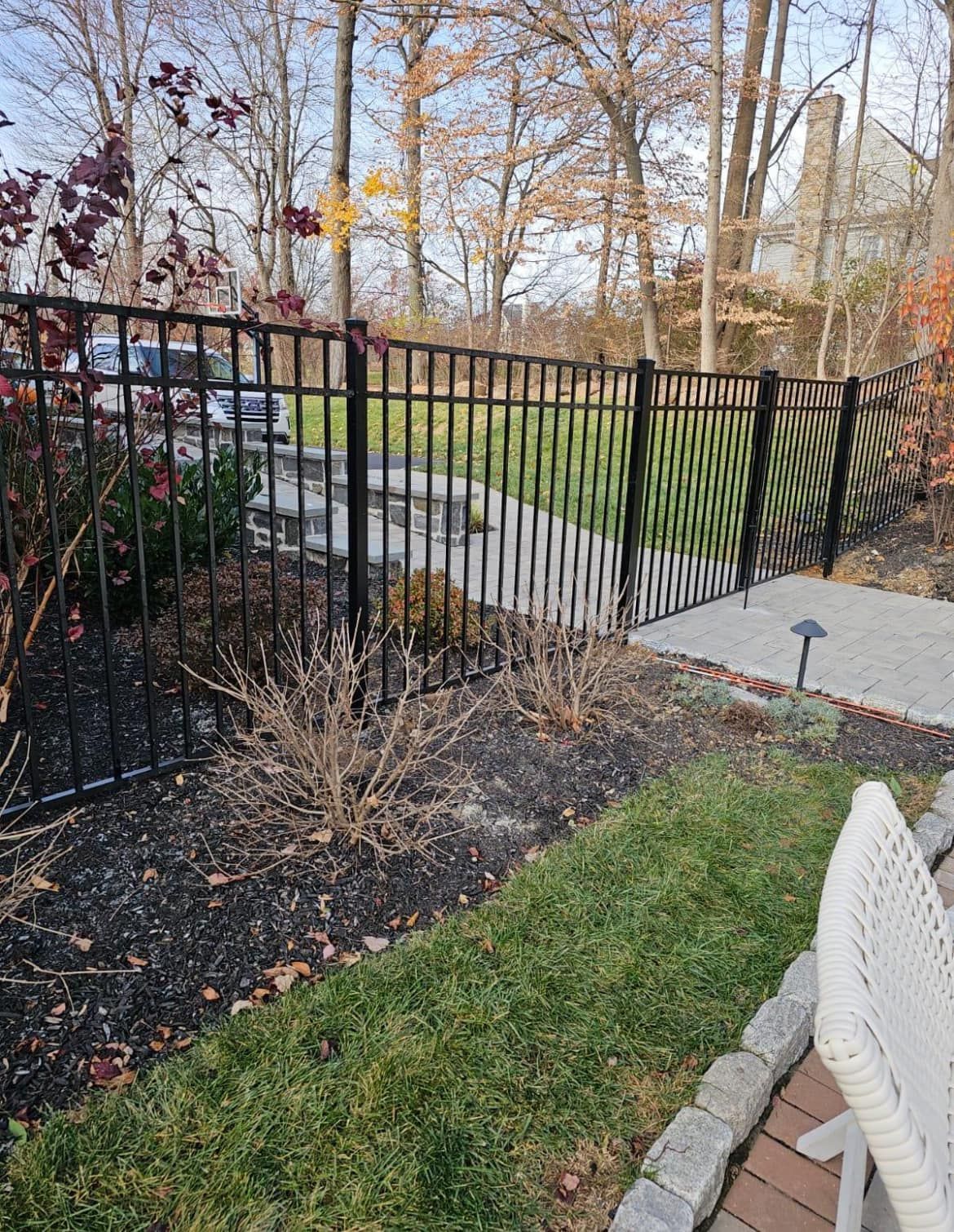 Black metal fence bordering a pathway and lawn, trees in the background.