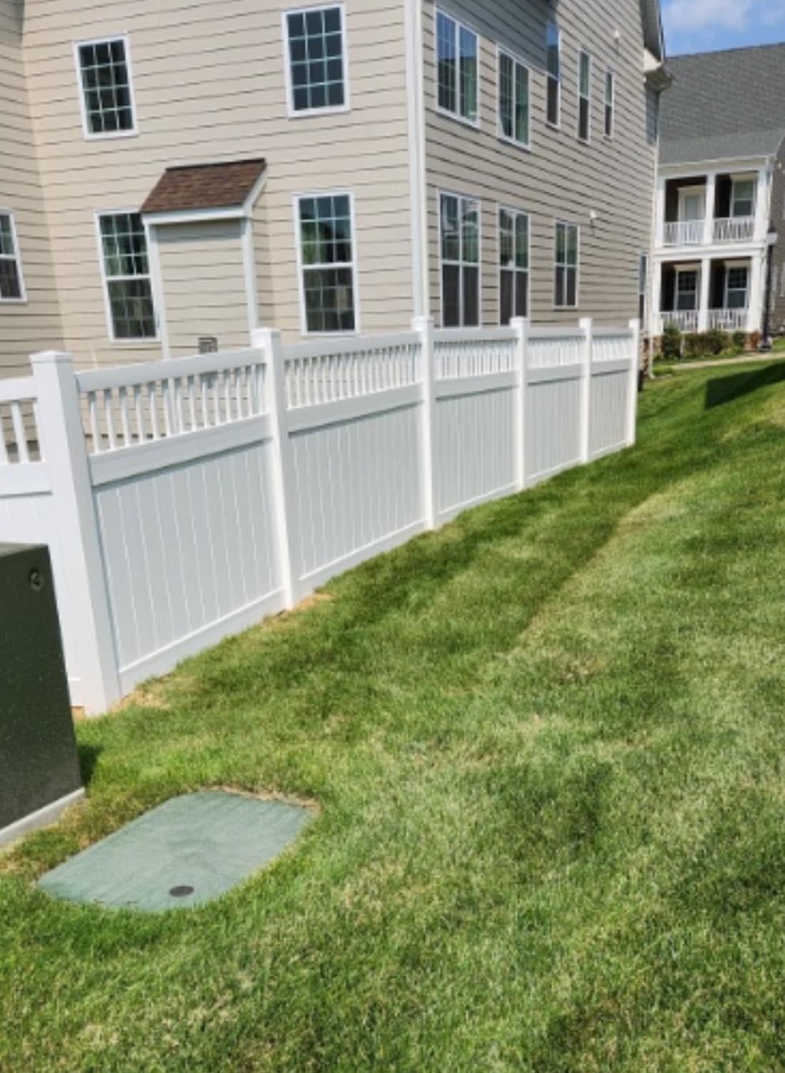 White vinyl fence bordering a grassy yard next to a two-story building.