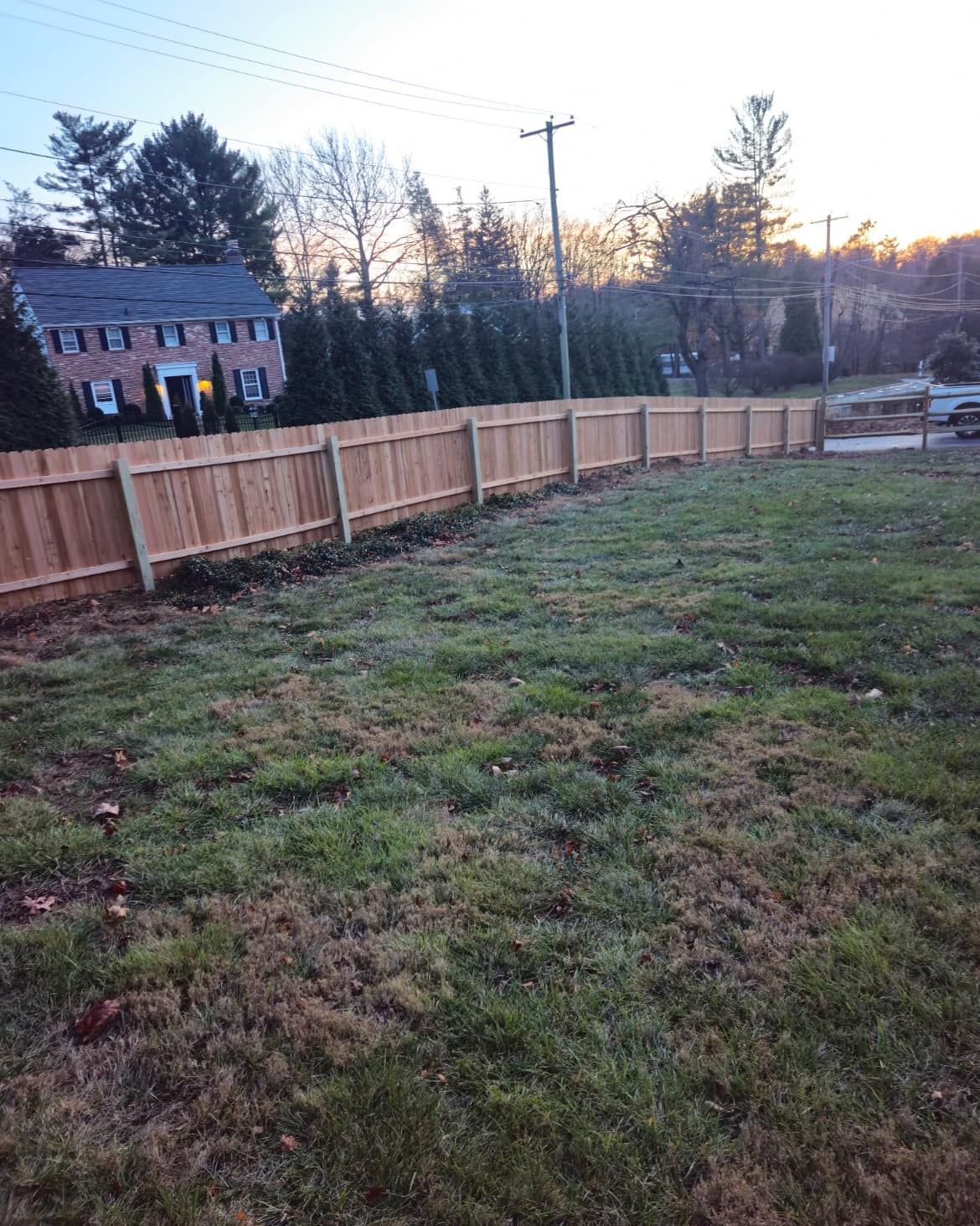 Wooden fence in a grassy yard, with a house in the background. Dusk light.