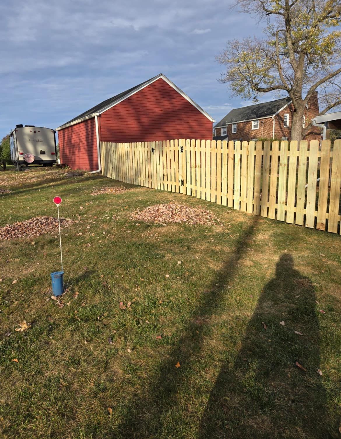Wooden fence along a yard, red barn in the background, shadow of a person, and a cloudy sky.
