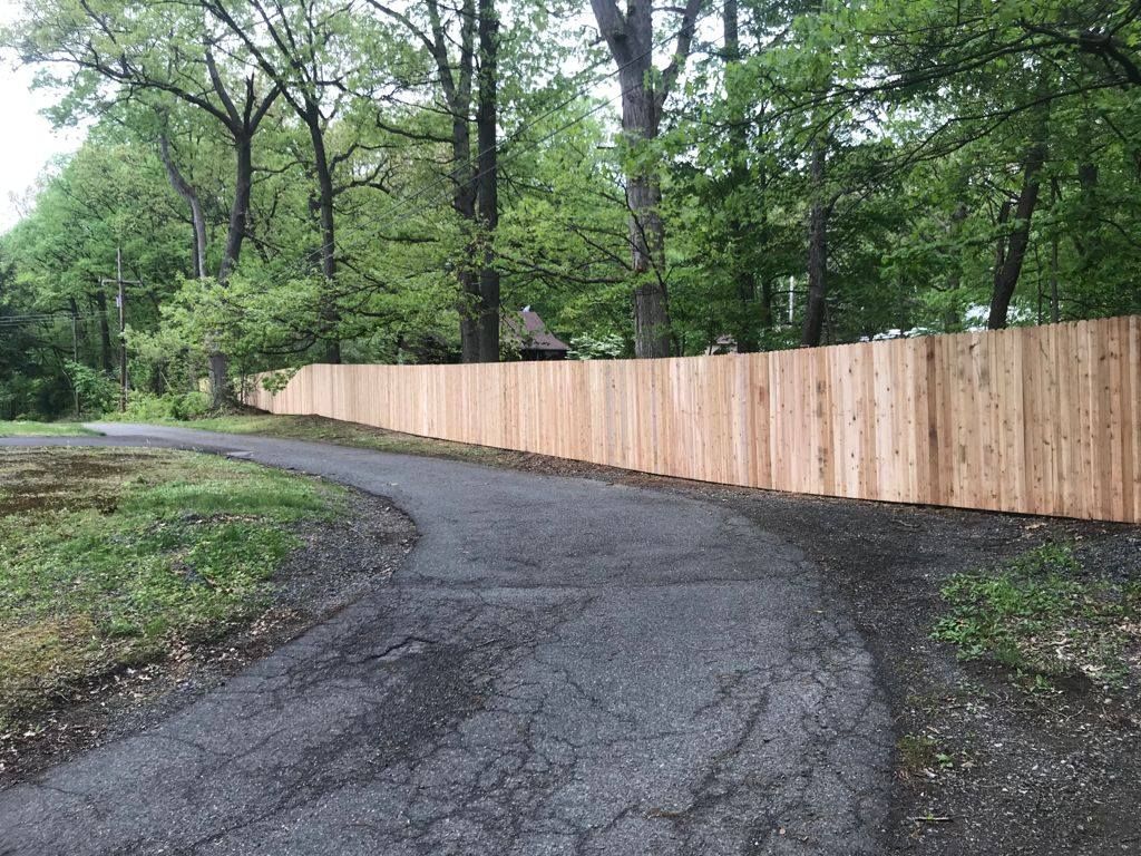 Wooden fence lines a curved asphalt path through a wooded area.