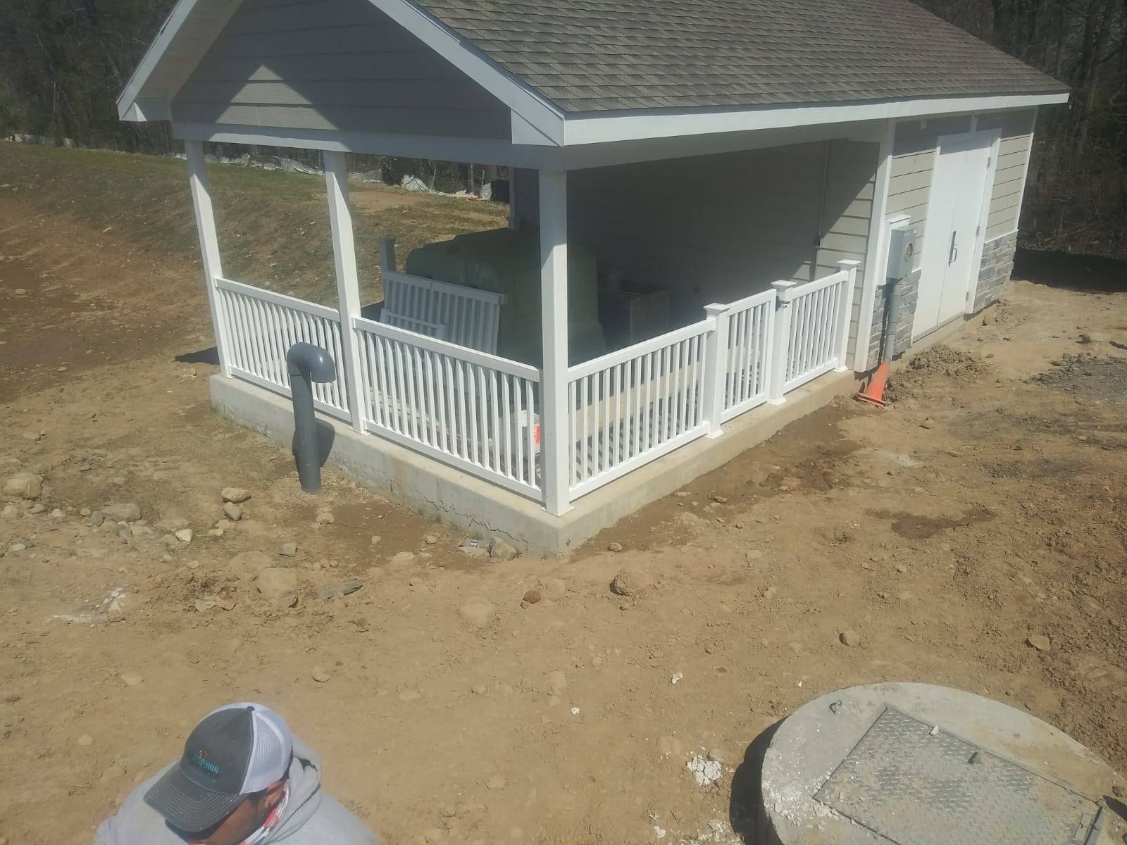Building with white railing and roof, next to a manhole and a man.