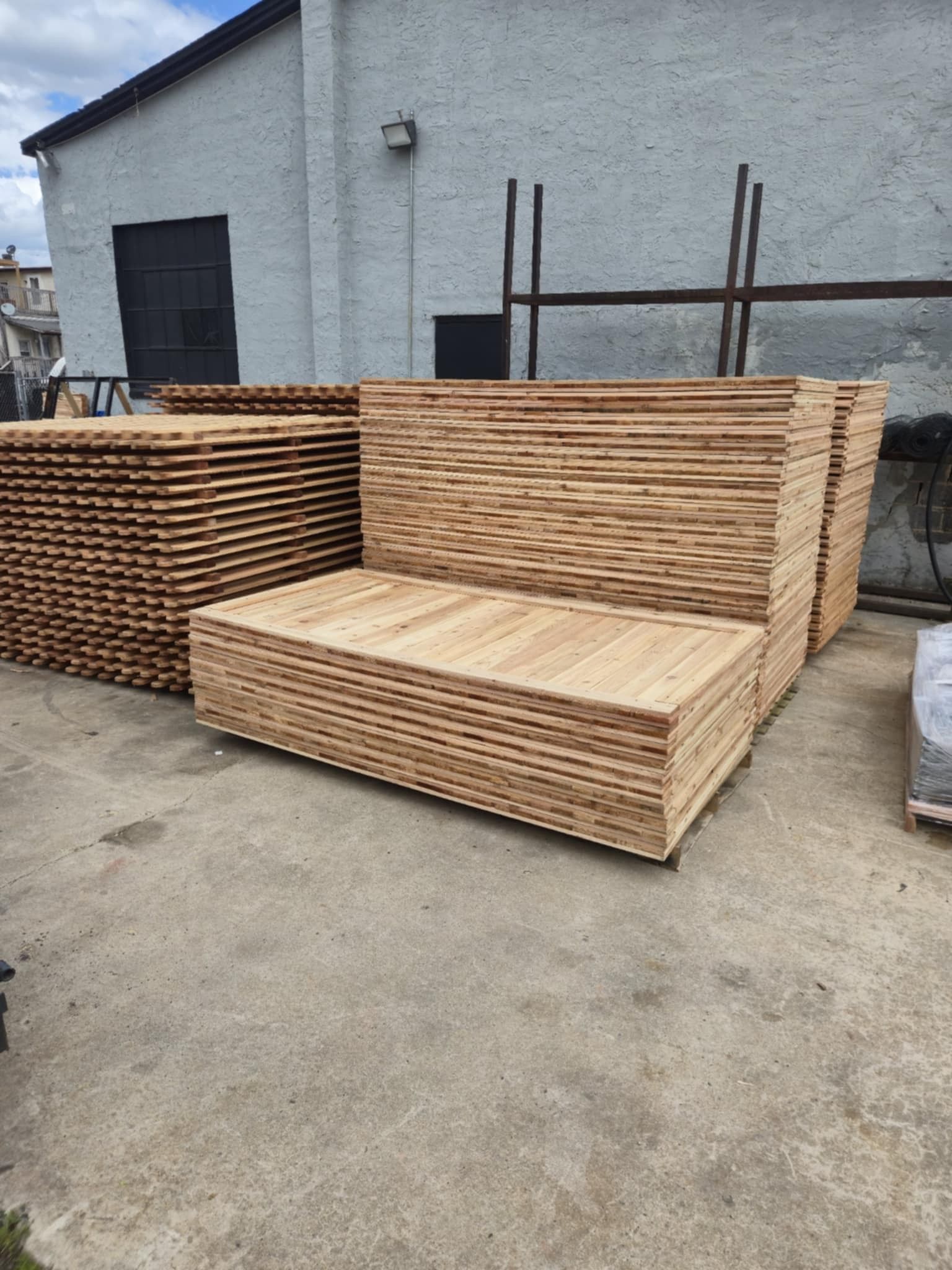 Stacks of lumber planks in front of a gray building.