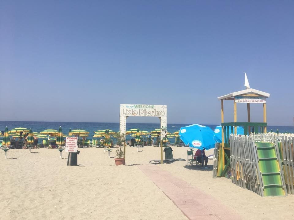 Spiaggia sabbiosa con ombrelloni, torretta di salvataggio e arco d'ingresso nelle giornate di sole.