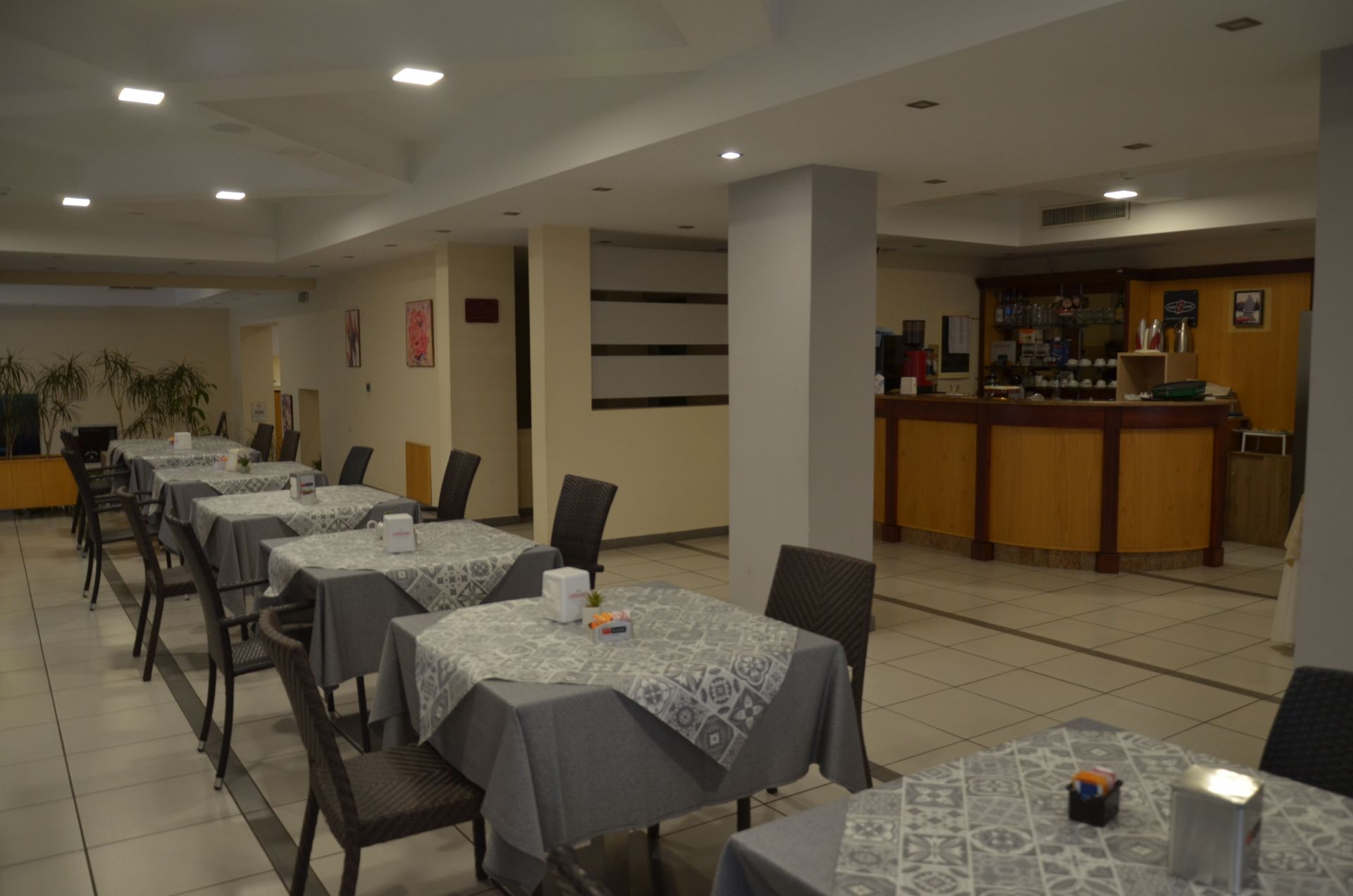 Sala da pranzo vuota del ristorante con tavoli apparecchiati per il servizio e un bar sullo sfondo.