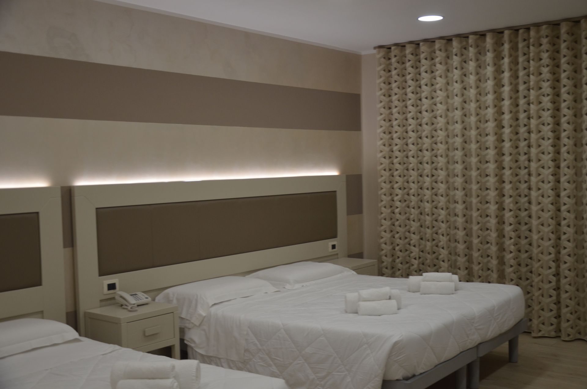 Camera d'albergo con tre letti, pareti beige e tende a fantasia.