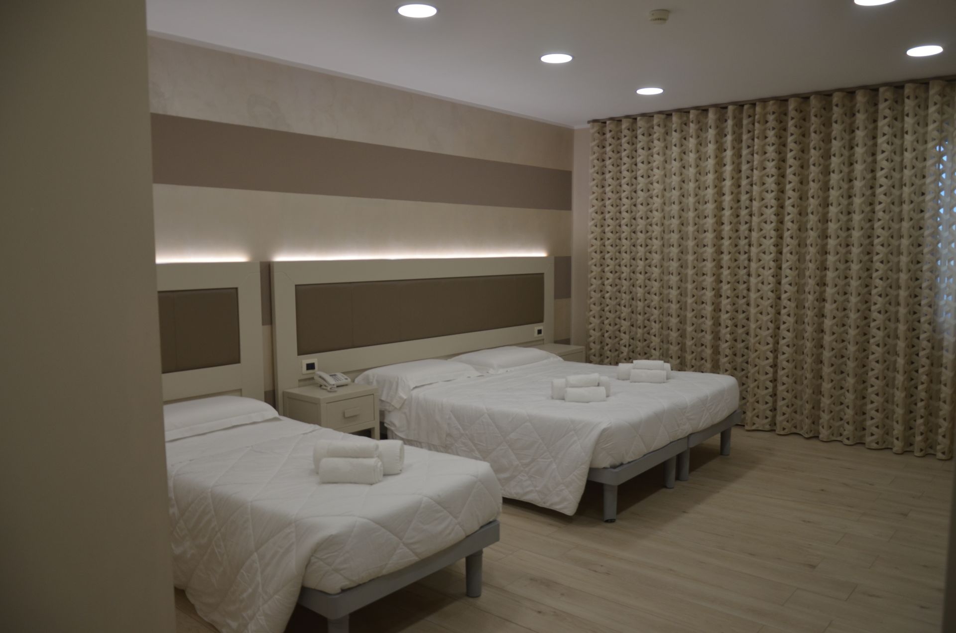 Camera d'albergo con due letti, pareti beige e tende a fantasia.