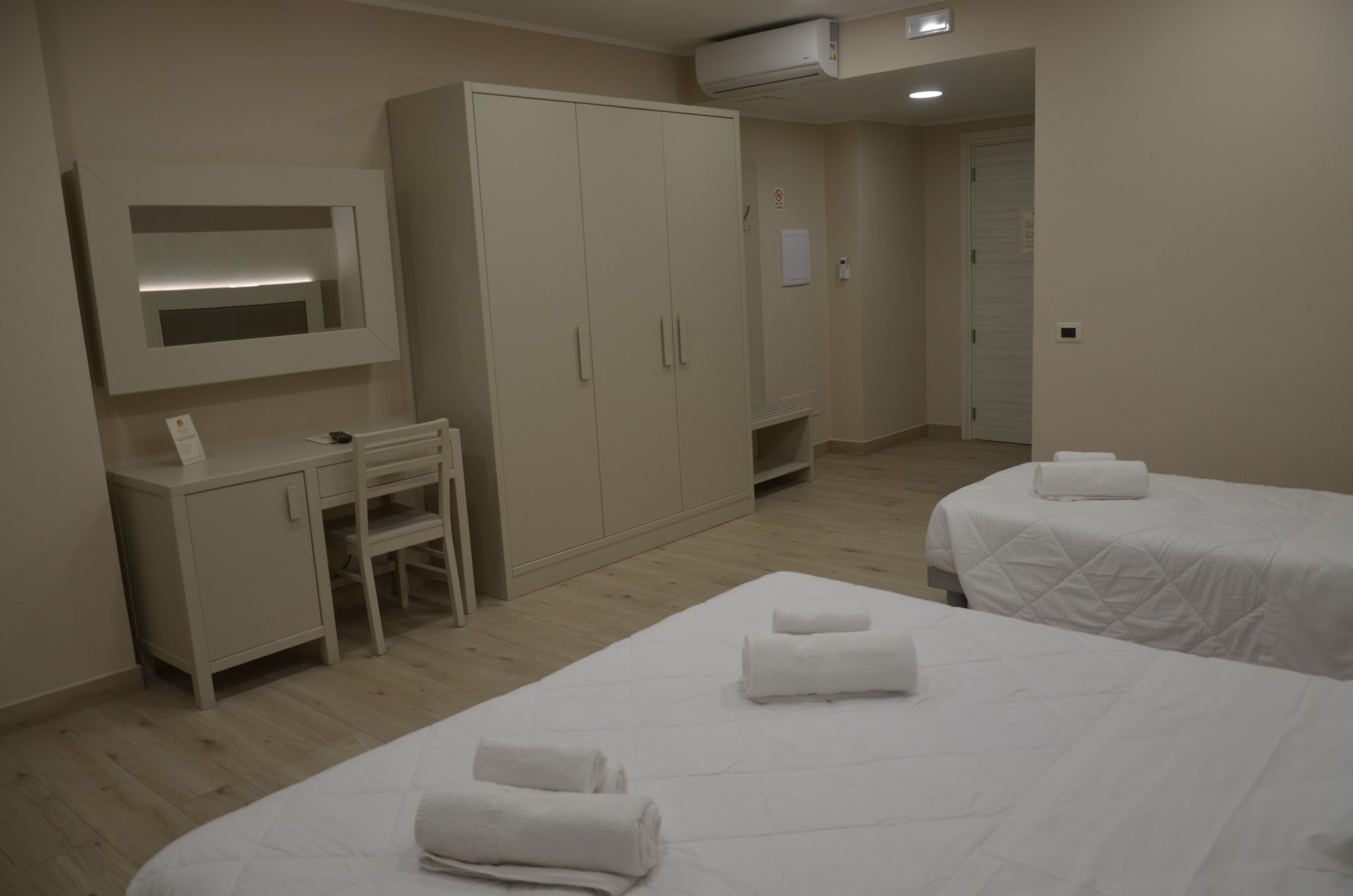 Camera da letto con tre letti, cassettiera, armadio e pareti bianche.