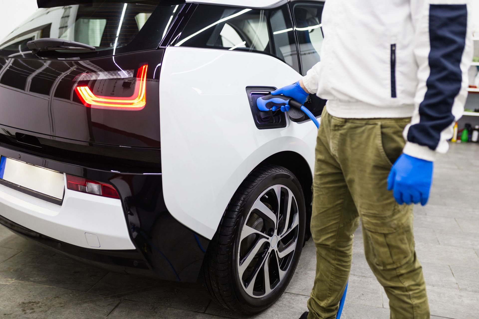 Persona che collega un veicolo elettrico (EV) a una stazione di ricarica. Veicolo elettrico bianco e nero, persona che indossa guanti blu.