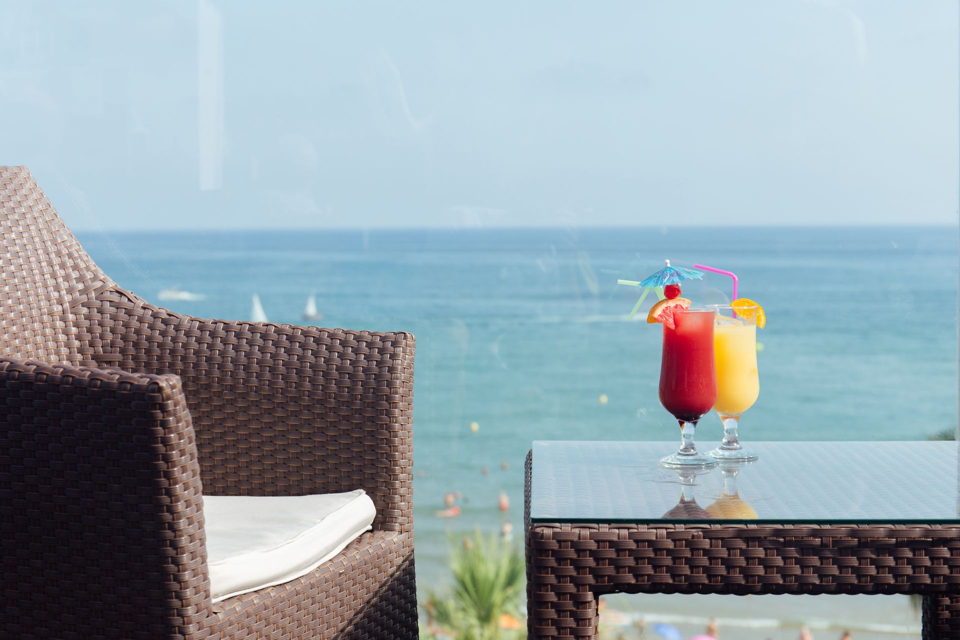 Sedia e tavolo in vimini con due cocktail colorati che si affacciano sull'oceano blu.
