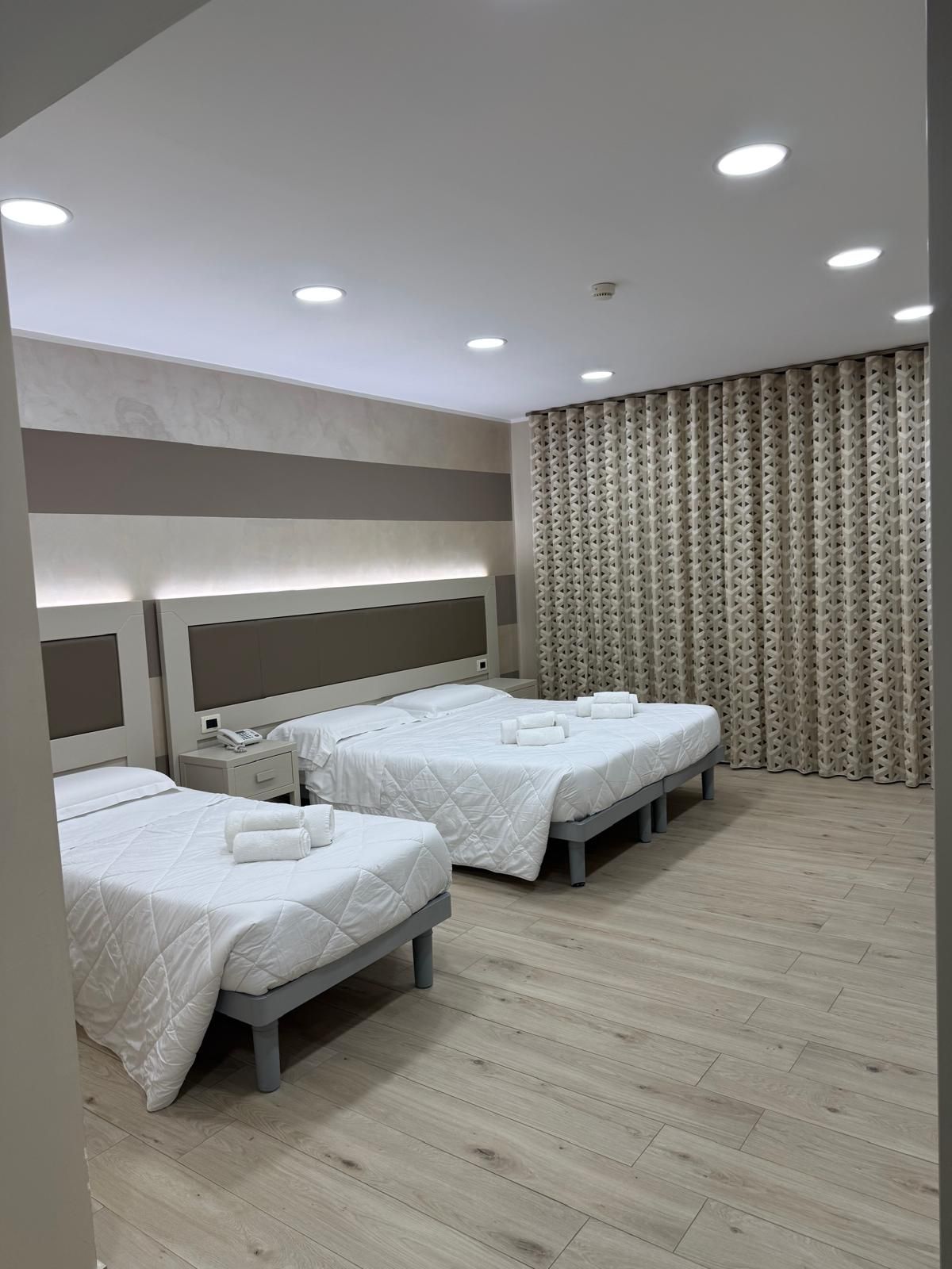 Camera d'albergo con tre letti, lenzuola bianche, pavimenti in legno chiaro e pareti dai toni neutri.