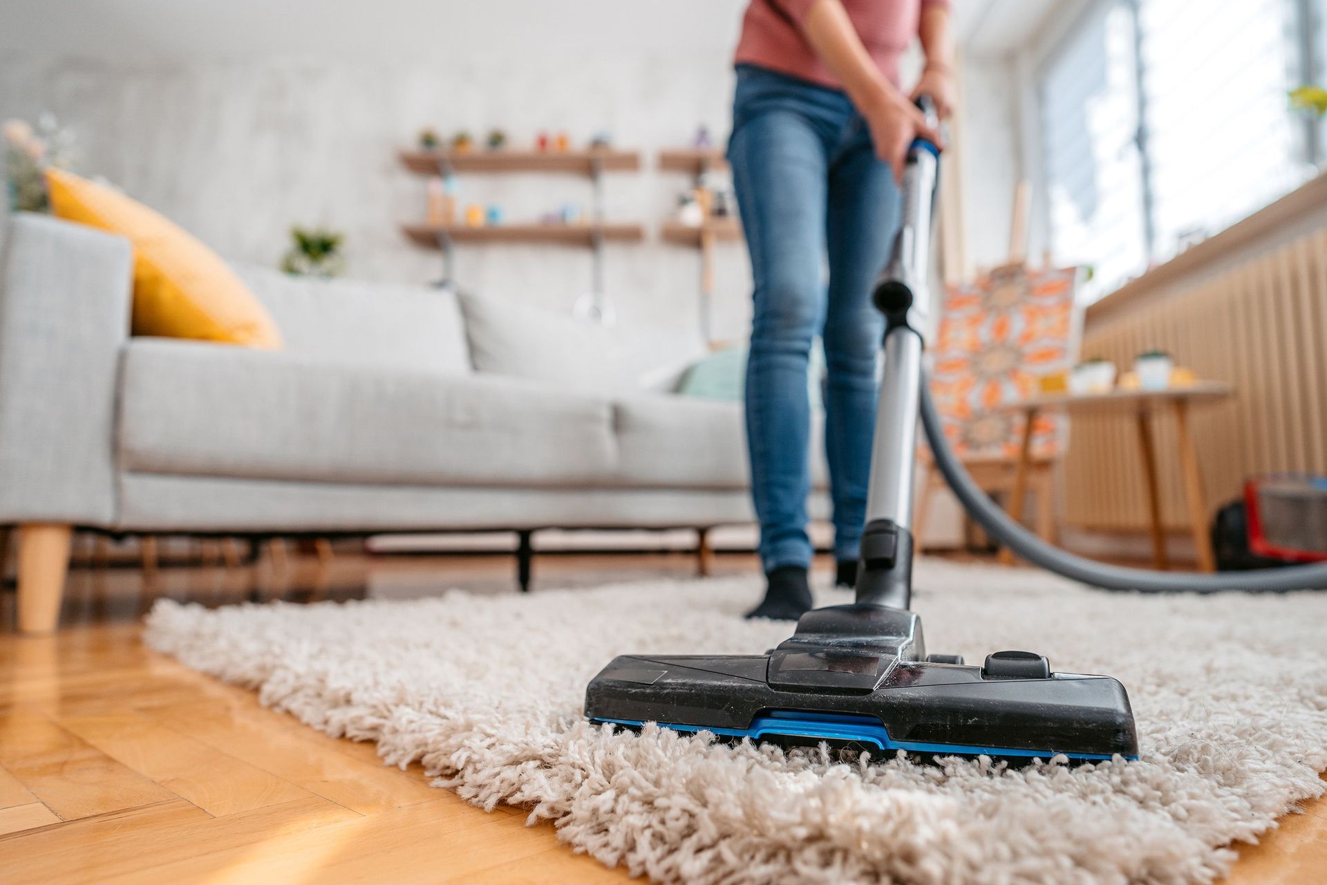 A person in jeans uses a vacuum cleaner on a thick, white shaggy rug in a living room.