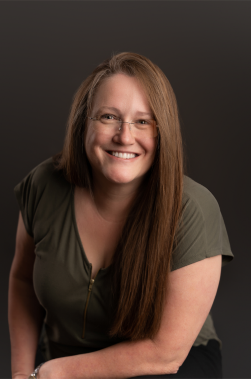 A woman wearing glasses and a green shirt is smiling for the camera.