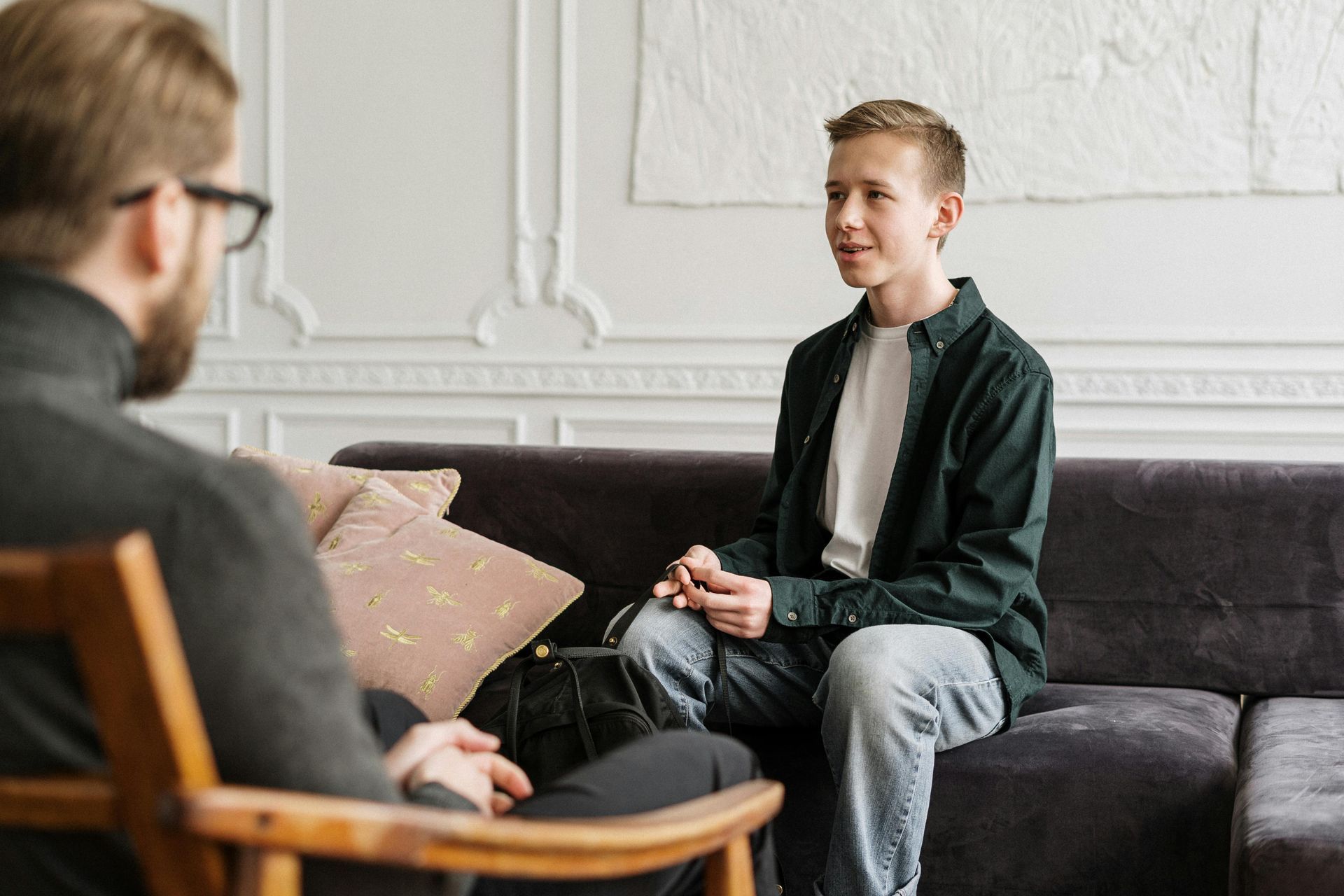 A man is sitting on a couch talking to another man.