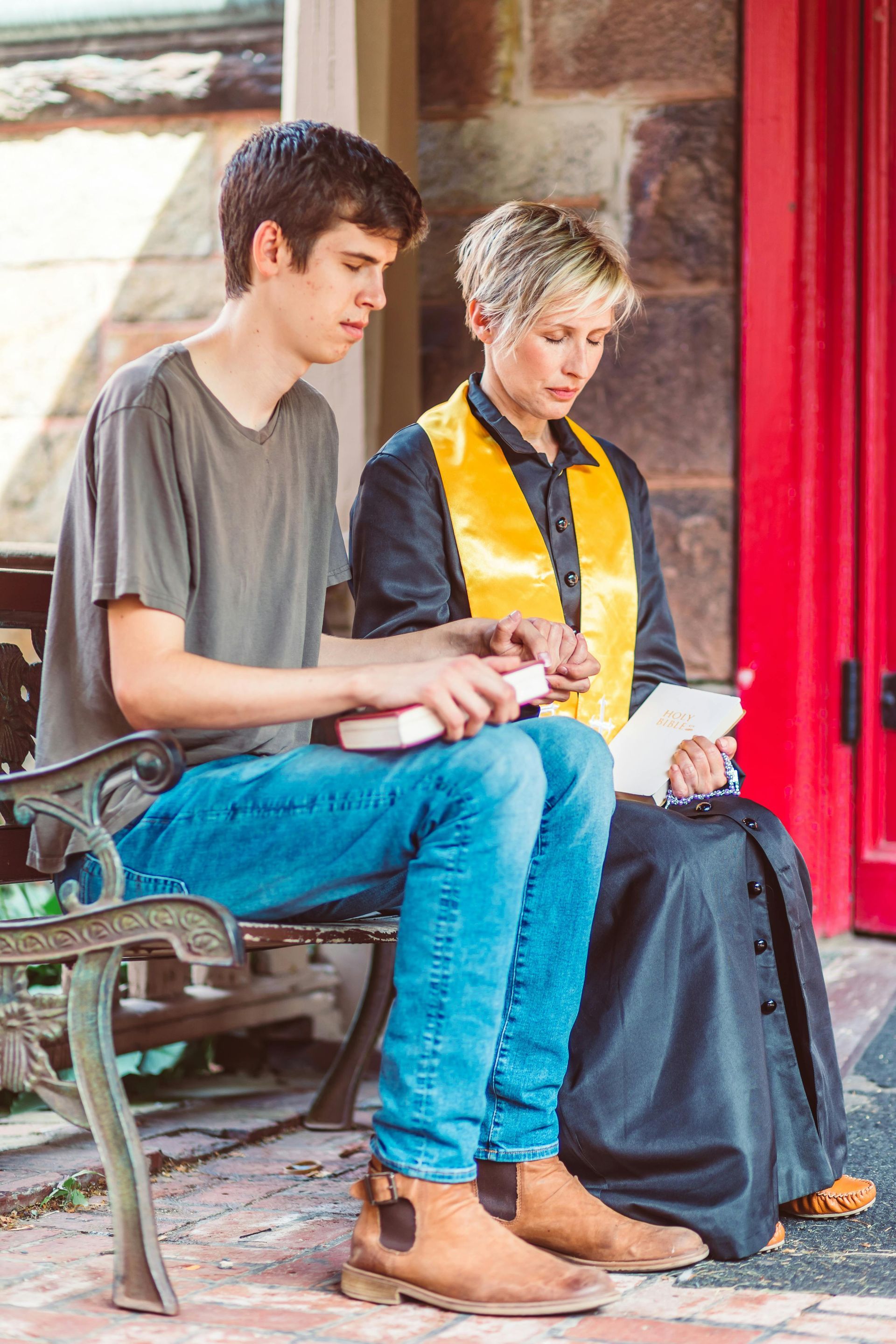 A man and a woman are sitting on a bench in front of a red door.