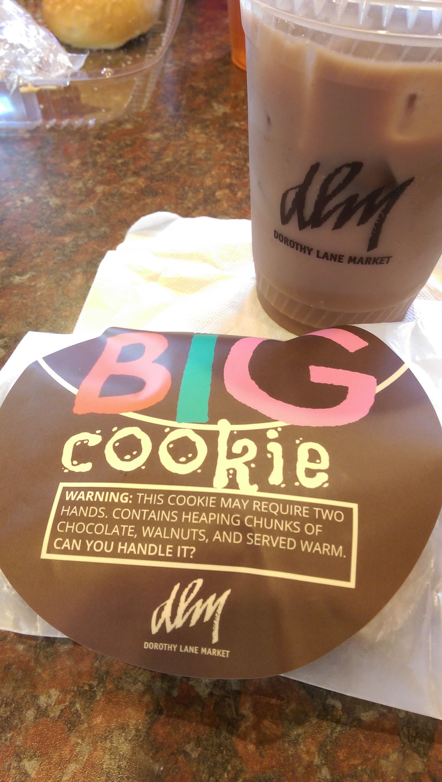 Big cookie with pink and green text, next to an iced coffee with the brand's logo on it.