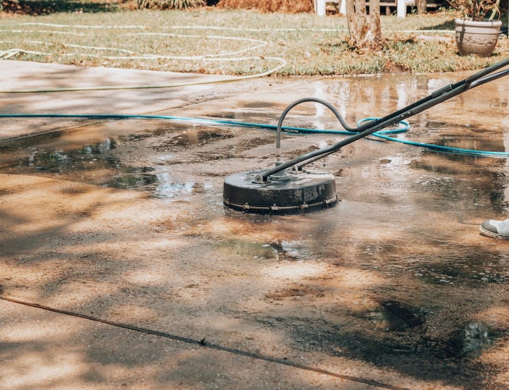A Person is Using a Machine to Clean a Concrete Driveway — Cleaning & Security in Port Douglas QLD— Cleaning & Security in Port Douglas QLD