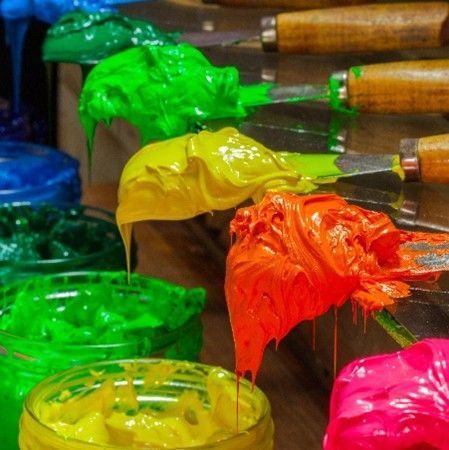 A row of jars filled with different colored paint and knives on a table.