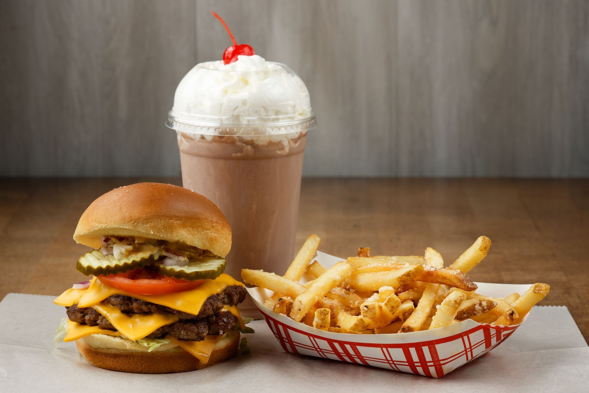 A hamburger , french fries and a milkshake on a table.