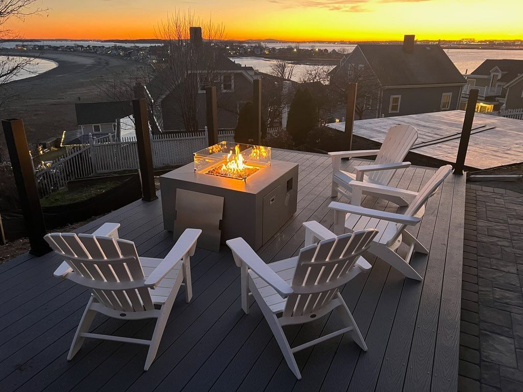 A deck with chairs and a fire pit at sunset.