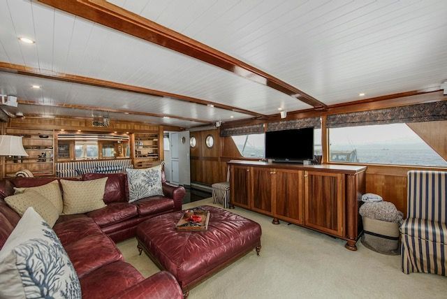 Living room on a yacht with red leather sofa, wood paneling, TV, and porthole view of ocean.