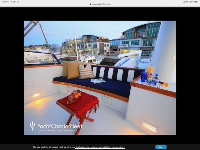 A yacht deck with blue and white cushions, a small table with fruit, and a coastal town view.