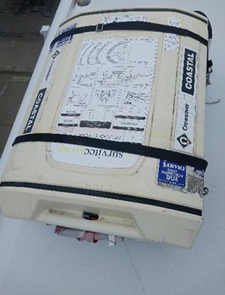 White and black Survitec coastal life raft, closed, on a white surface.