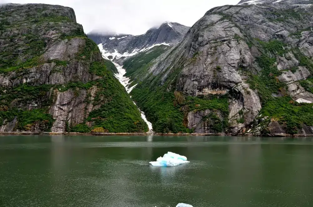 A luxury yacht's deck with a dinghy, equipment, and a city harbor in the background at sunset.