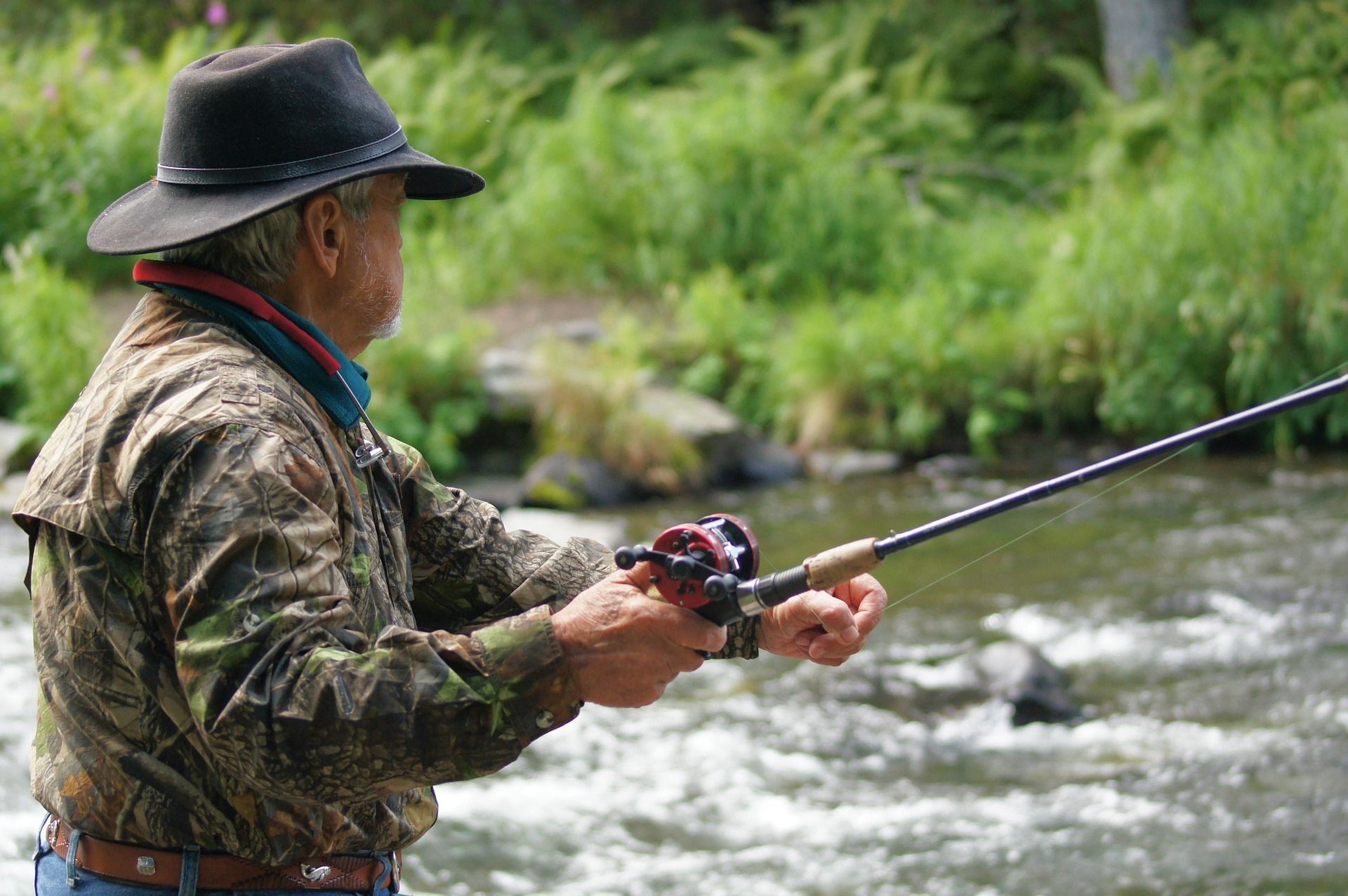 Man in camo shirt and hat fishing in a river.