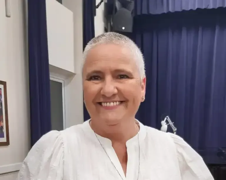A woman in a white shirt is smiling in front of a blue curtain.