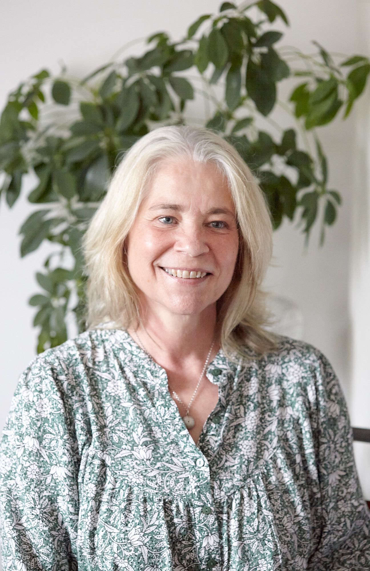 A woman with a green dress on smiling at the camera with a plant behind her