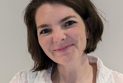 A woman with short brown hair is smiling and wearing a white shirt.