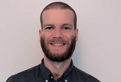A man with a beard is smiling for the camera while wearing a blue shirt.